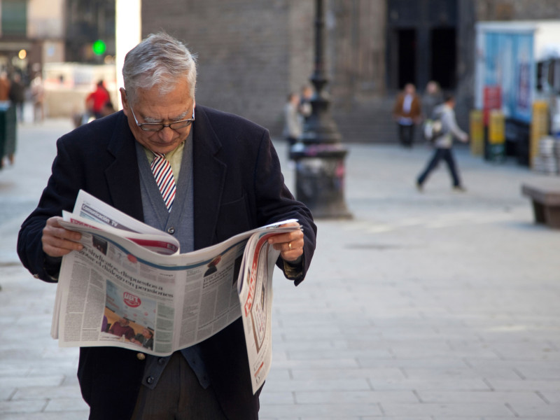 Un anciano lee el periódico en las calles del antiguo Barrio Gótico de Barcelona, España